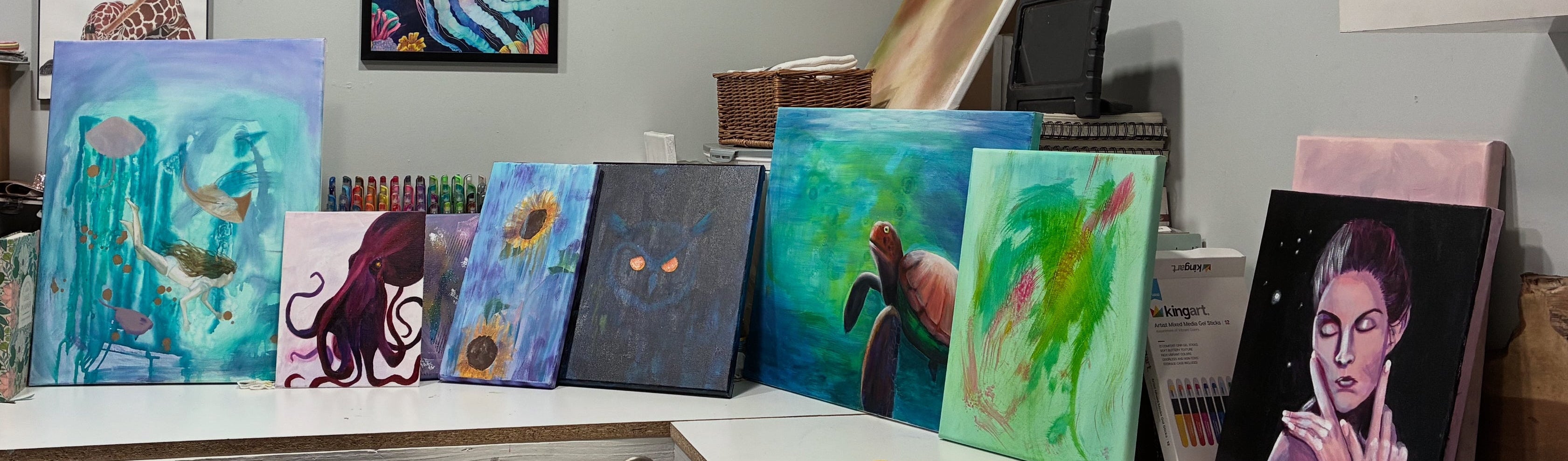 Art studio with various paintings on a table and on the wall.